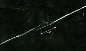 Calcite veins (white) in a cut and polished surface of a tile of black marble building stone from Italy. The thicknesses of the veins vary from hairline to about 3.5 mm. Two segments of the veins overlap for about 5 cm, which, together with large thickness variation, reveals multi-stage opening history. Sample courtesy of Isik Aydinli.